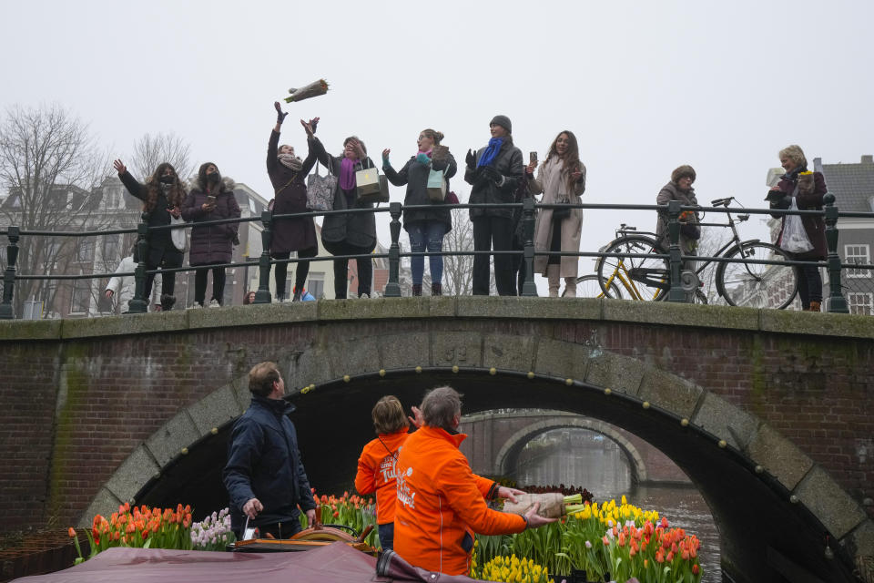 People catch free bouquets of tulips in Amsterdam, Netherlands, Saturday, Jan. 15, 2022, as stores across the Netherlands cautiously re-opened after weeks of coronavirus lockdown, and the Dutch capital's mood was further lightened by dashes of color in the form of thousands of free bunches of tulips handed out by growers sailing with a boat through the canals. (AP Photo/Peter Dejong)
