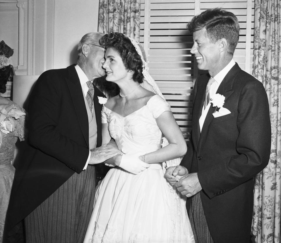<p>Ex-ambassador Joseph P. Kennedy kisses his new daughter-in-law Jackie Kennedy on the cheek during her wedding reception in Newport, Rhode Island as the bridegroom, Senator John F. Kennedy looks on.</p>