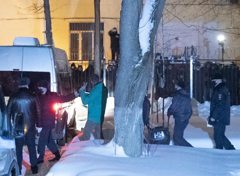 An opposition leader Alexei Navalny, centre, signals to onlookers as he is escorted hand-cuffed after a court hearing in Moscow, Russia, Monday, Jan. 18, 2021. A judge has ordered that Alexei Navalny be held in custody for 30 days, his spokeswoman Kira Yarmysh said on Twitter. The ruling Monday concluded an hours-long court hearing set up at a police precinct where the politician has been held since his arrest at a Moscow airport Sunday. (AP Photo/Pavel Golovkin)