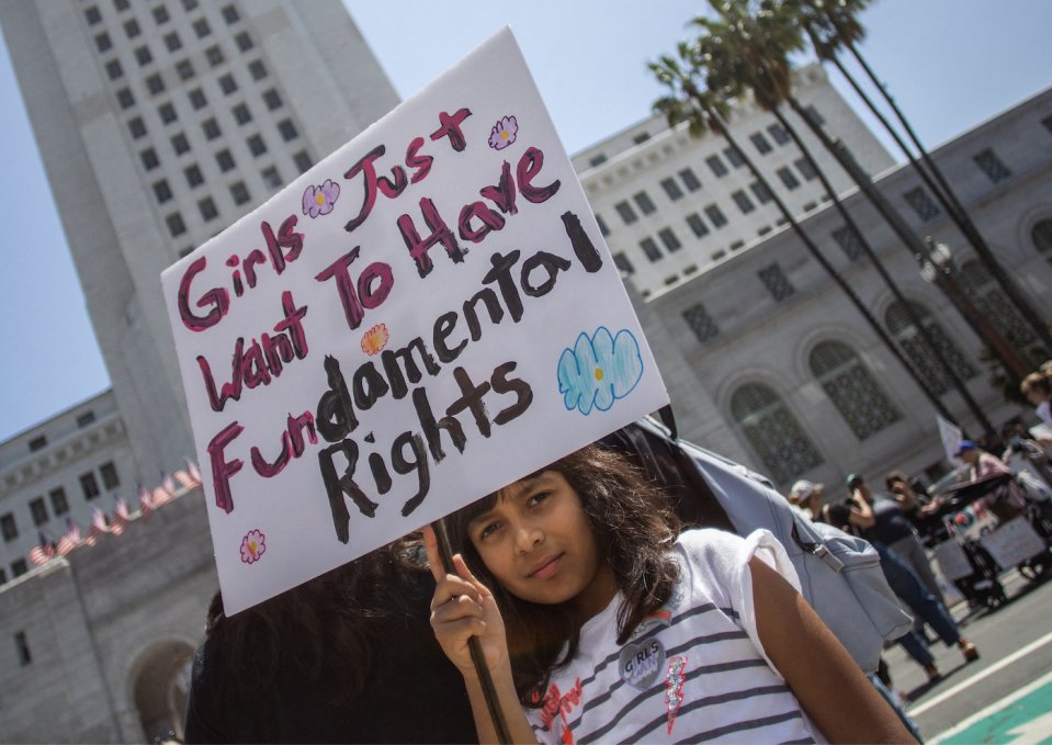 A young girl holding up a protest sign that says "Girls just want to have fundamental rights."