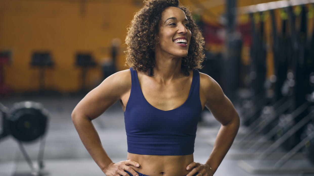  Strong woman smiling in gym with hands on her hips. 