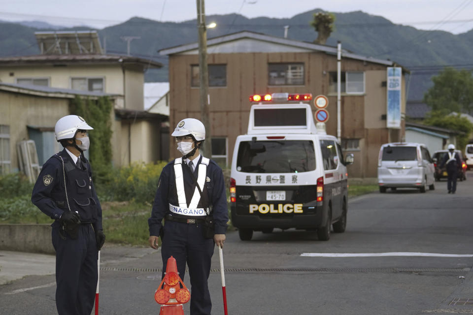 Police officers stand guard on a street leading to a building where a man is holed up in Nakano, central Japan, Thursday, May 25, 2023. A masked man carrying a rifle and a knife was holed up in a building Thursday in Nakano, a city of Nagano prefecture. Multiple people were injured, one of whom later died, police said. (Kyodo News via AP)