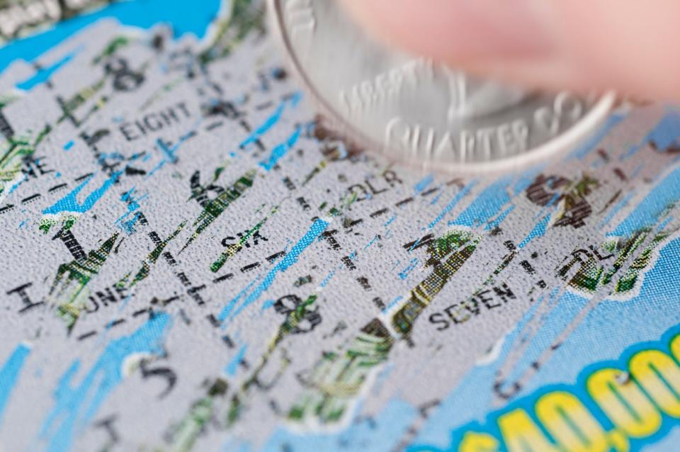 close up of lottery ticket being scratched with silver coin held between two fingers