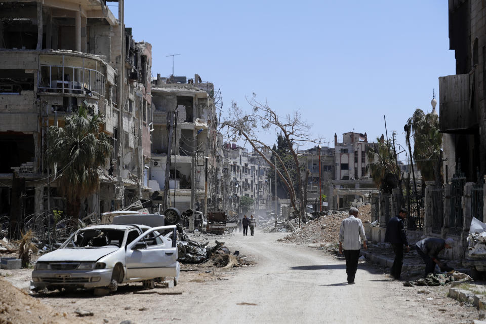 FILE - Syrians walk through destruction in the town of Douma, the site of a suspected chemical weapons attack, near Damascus, Syria, Monday, April 16, 2018. French judicial authorities on Wednesday issued international arrest warrants for Syrian President Bashar Assad, his brother Maher, and two army generals alleging their involvement in war crimes and crimes against humanity, including in chemical attacks in 2013 on rebel-held Damascus suburbs, lawyers for Syrian victims said. (AP Photo/Hassan Ammar, File)