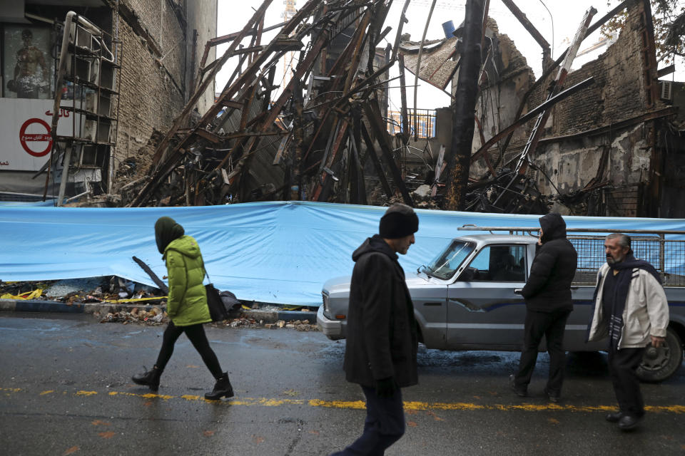 FILE - In this Nov. 20, 2019 file photo, people walk past buildings that were burned during recent protests, in Shahriar, Iran. While the 2011 Arab Spring uprisings that took place in Egypt, Tunisia, Libya and Syria were directed at long-ruling autocrats, the current economically driven uprisings are directed at corrupt political elites who have failed at providing their people with basic services. In Iran, economic discontent has worsened since President Donald Trump imposed crushing sanctions last year. (AP Photo/Vahid Salemi, File)