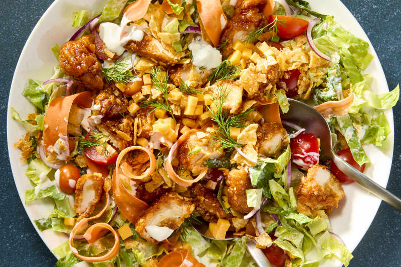 An overhead view of sticky chicken salad on a white plate on a green background with a spoon digging in.