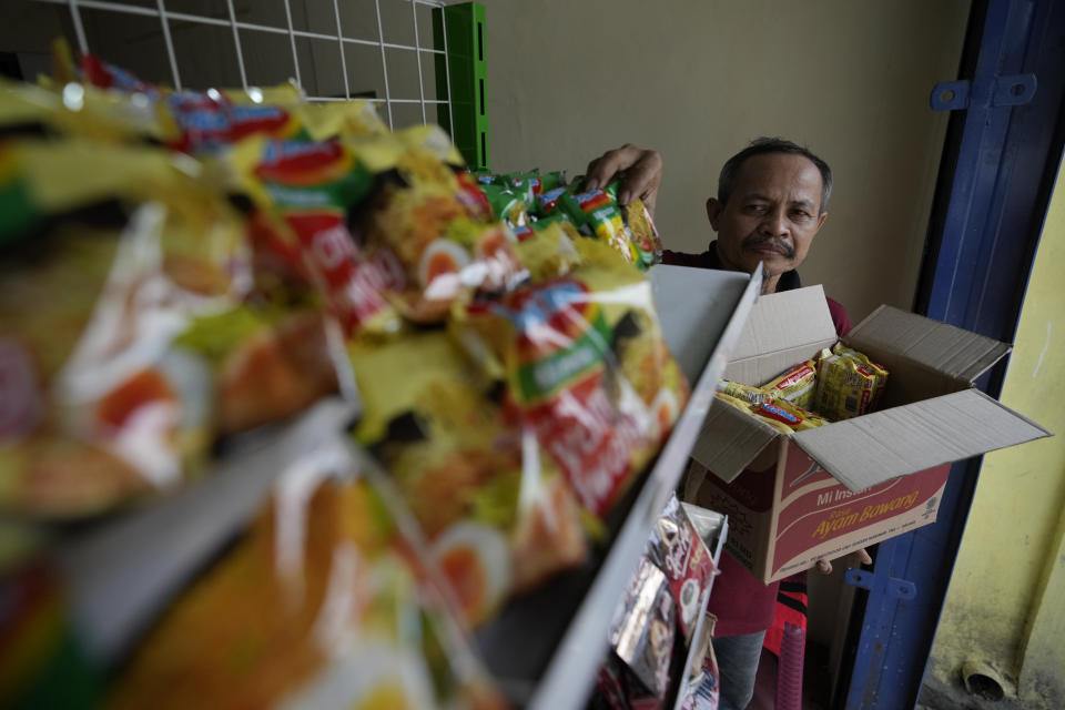 Mukroni, 52, places instant noodles on a shelf at his store in Bekasi, on the outskirts of Jakarta, Indonesia, Thursday, Feb 2, 2023. Nearly a year after Russia invaded Ukraine, punishingly high food prices are inflicting particular hardship on the world’s poor. Customers, Mukroni said, “will not come to the shop’’ if prices are too high. (AP Photo/Achmad Ibrahim)