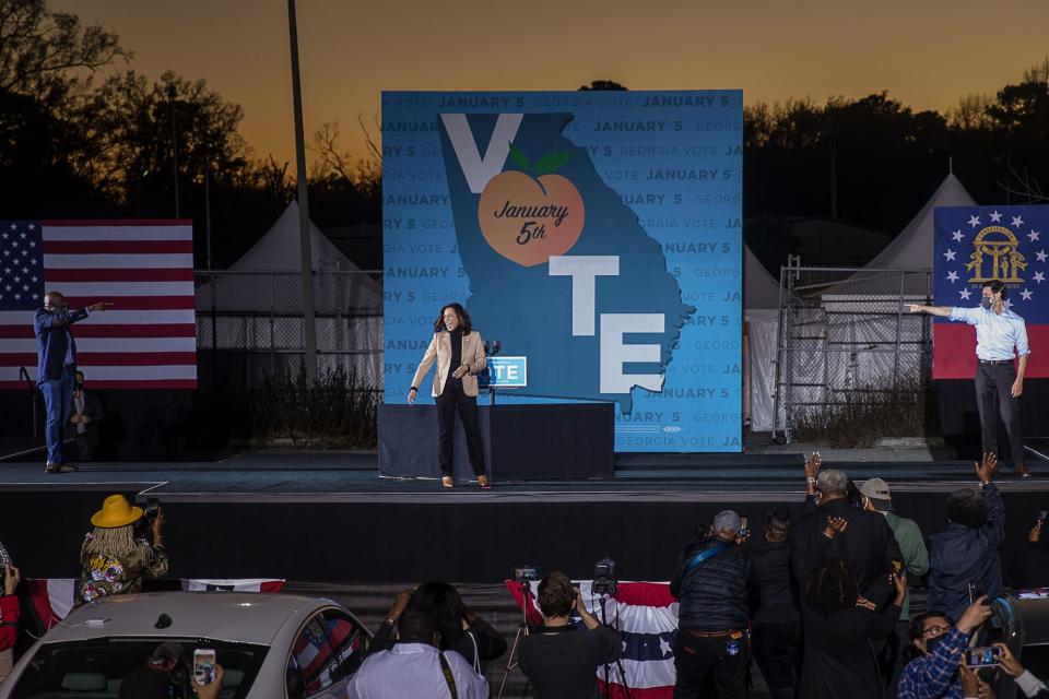 Senate candidates Rev. Raphael Warnock and Jon Ossoff point toward Vice President-elect Kamala Harris during a campaign event at Garden City Stadium.