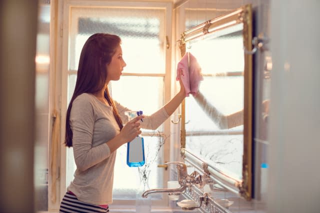 Young woman cleaning mirror in the bathroom.