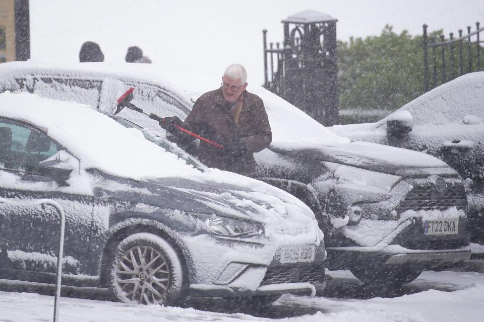 A person clears snow from a parked car in Buxton, Peak District (PA)