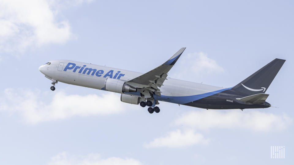 A Prime Air cargo jet with light blue lettering and dark blue tail takes off into blue sky with white clouds.