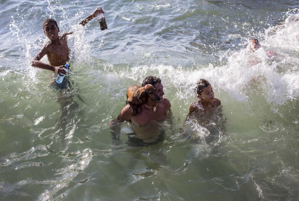 FILE - In this July 22, 2018 file photo, a man's pet dog stands on his shoulder as they take a dip in the ocean with other swimmers near Playita 16 in Havana, Cuba. (AP Photo/Desmond Boylan, File)