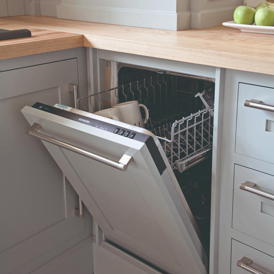 An open dishwasher in a light grey kitchen with silver hardware