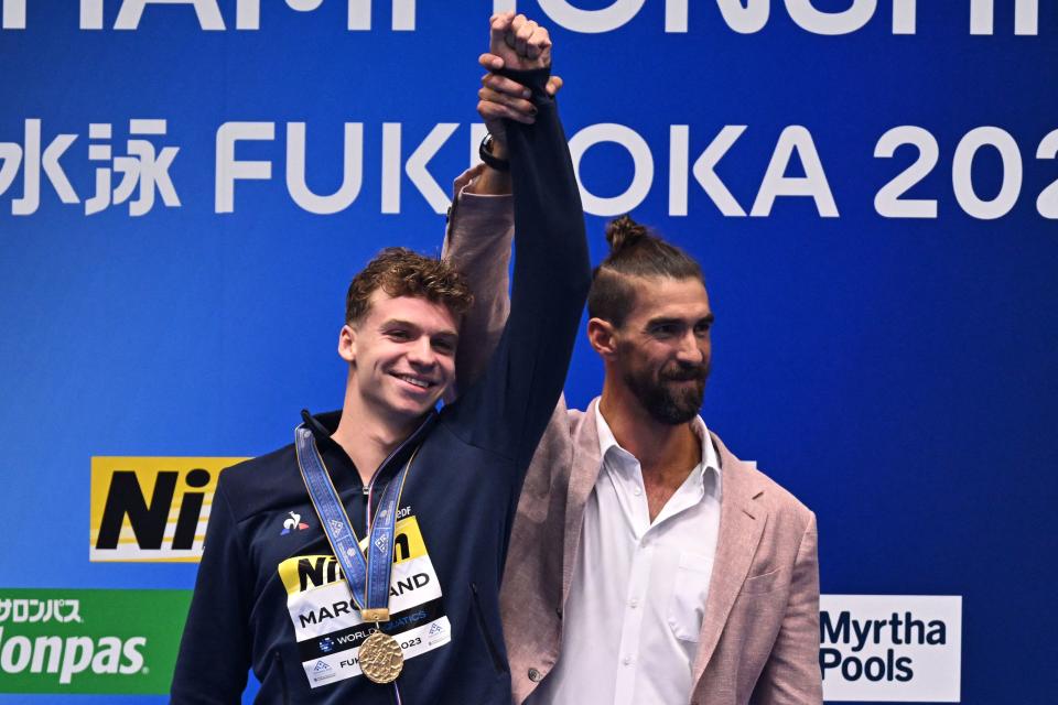 El multimedallista olímpico Michael Phelps (derecha) levanta el brazo de Léon Marchand durante la premiación de los 400 metros estilo medley en el Campeonato del Mundo de Fukuoka 2023. (Foto: MANAN VATSYAYANA/AFP via Getty Images)