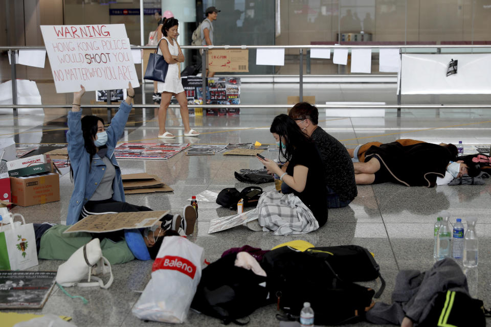 A protester shows a placard to travellers as they continue their sit-in rally at the airport in Hong Kong, Wednesday, Aug. 14, 2019. Flight operations resumed at the airport Wednesday morning after two days of disruptions marked by outbursts of violence highlighting the hardening positions of pro-democracy protesters and the authorities in the Chinese city that's a major international travel hub. (AP Photo/Vincent Thian)