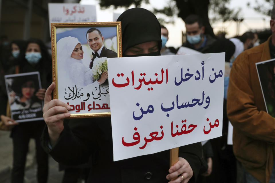 Relatives of the victims of the Aug. 4, 2020 Beirut port explosion hold portraits of their loved ones who were killed, Thursday, Feb. 4, 2021 in Beirut, Lebanon. The vigil at the seaport main entrance, marked six months since the blast that killed more than 200 people and injured thousands. The Arabic words on poster read "Who brought nitrates and for who? We have a right to know." (AP Photo/Bilal Hussein)