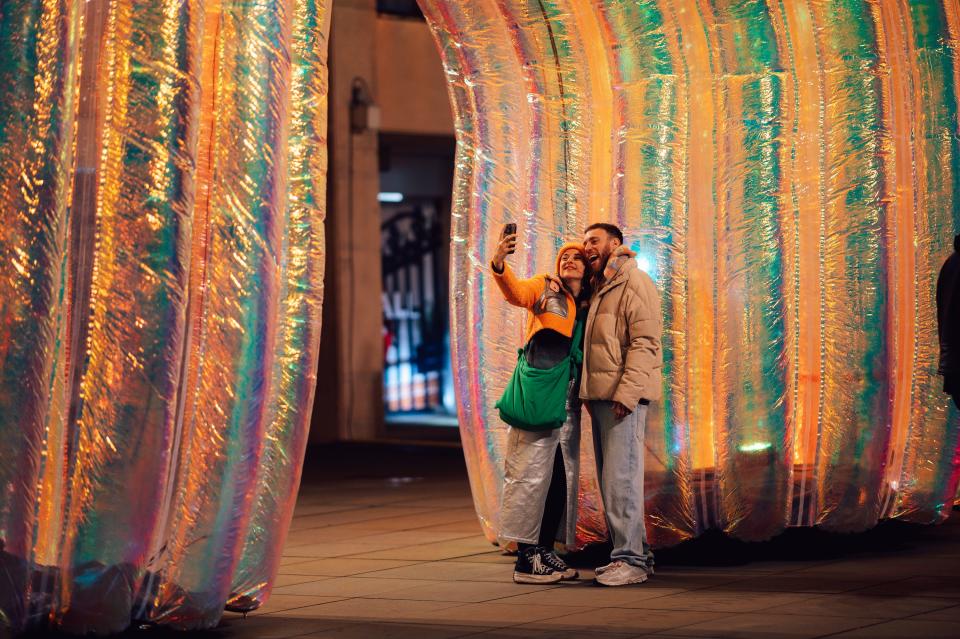 Two people take a photo under the Elysian Arcs installation at night. Photography by Chris Cooper/ ShotAway/ www.ShotAway.com/ #shotawaydotcom