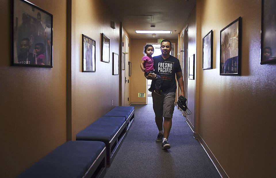 In this May 4, 2018 photo, Vanna In carries his daughter Thanny in Fresno, Calif. California Gov. Jerry Brown announced Friday, Aug. 17, 2018, he pardoned three former prisoners facing the threat of deportation to Cambodia, including Vanna In, who became a youth pastor after serving six years in the 1990s for murdering a rival gang member. (Eric Paul Zamora/The Fresno Bee via AP)