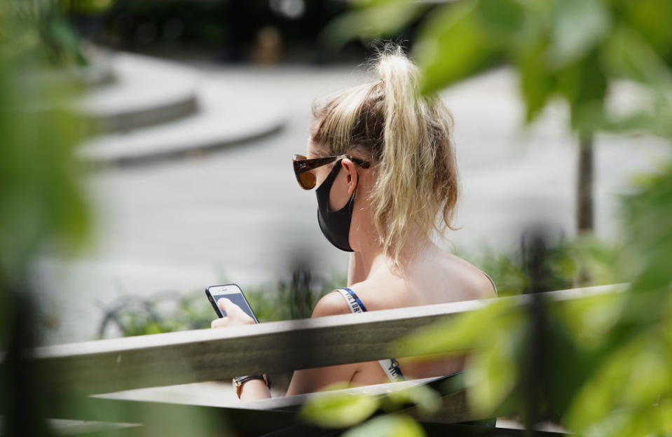 A woman sits on a park bench in New York looking at her phone. Source: Getty