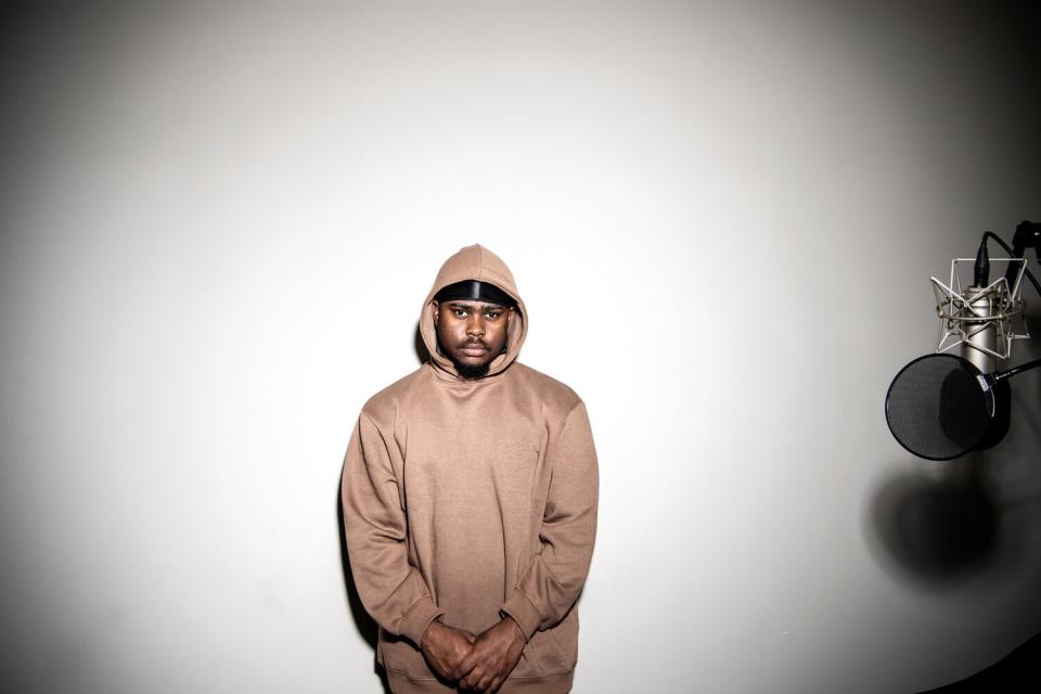 A man in a pink-brown sweatshirt in front of a white wall