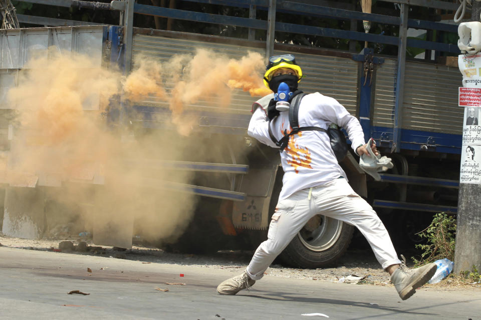 FILE - In this March 27, 2021, file photo, an anti-coup protester throws a smoke bomb against police crackdown in Thaketa township Yangon, Myanmar. The military takeover of Myanmar early in the morning of Feb. 1 reversed the country's slow climb toward democracy after five decades of army rule. But Myanmar's citizens were not shy about demanding their democracy be restored. (AP Photo/File)