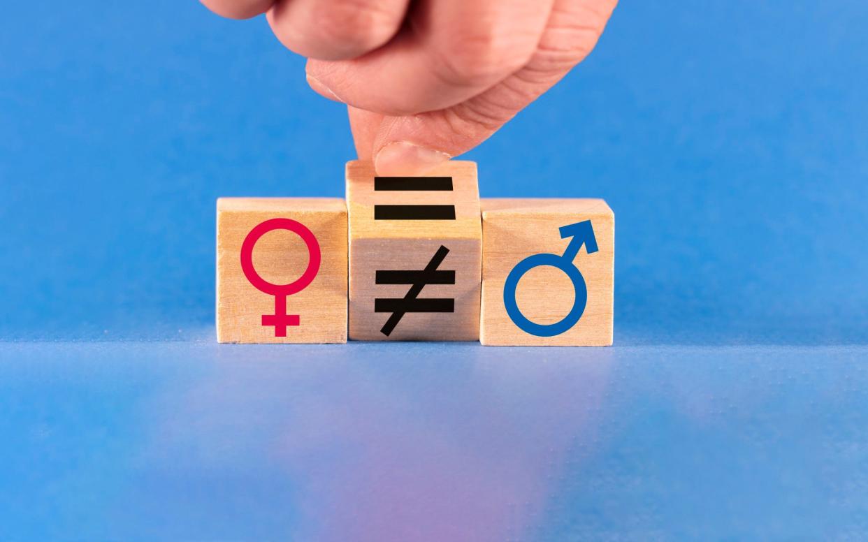 A hand turns a wooden die to change an unequal sign to an equal sign between male and female symbols on a blue background.