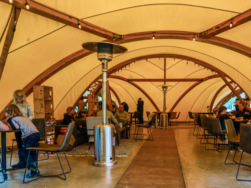 People converse at tables inside a large tent with yellow lighting