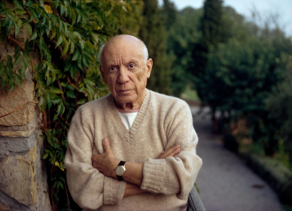 Pablo Picasso standing in a park with his arms crossed