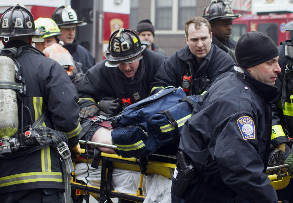 Firefighters and emergency medical personnel rush a firefighter from the scene of a multi-alarm fire at a four-story brownstone in the Back Bay neighborhood near the Charles River, Wednesday, March 26, 2014, in Boston. Boston EMS spokesman Nick Martin says four people, including at least three firefighters, have been taken to hospitals. (AP Photo/Scott Eisen)