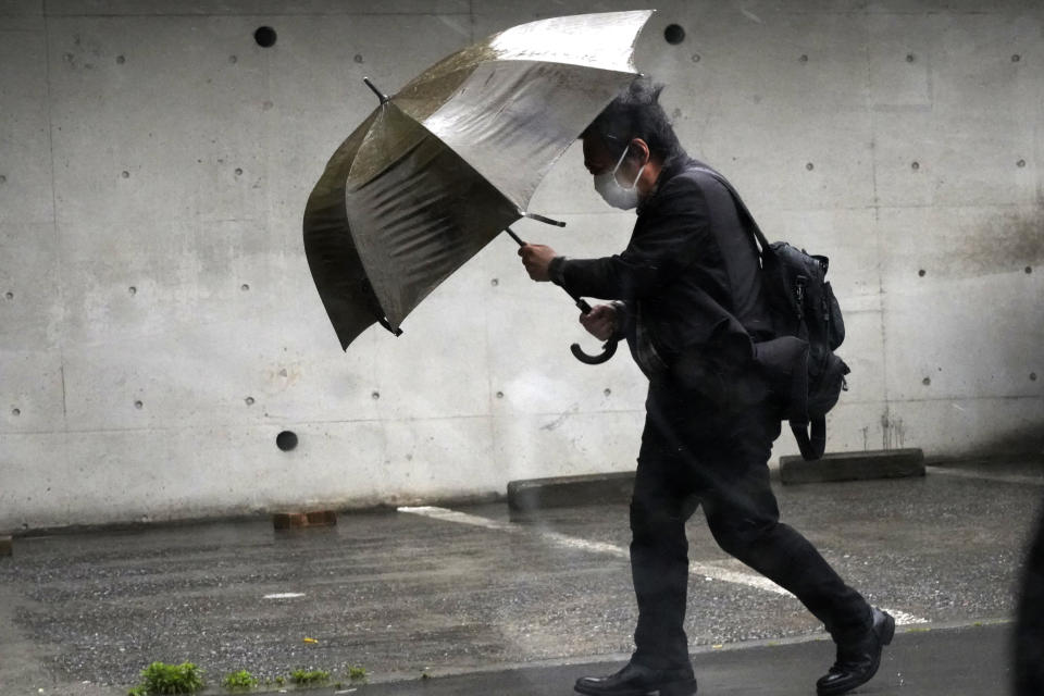 A person holds an umbrella against strong wind and rain as he walks on a street Friday, June 2, 2023, in Tokyo, as a tropical storm was approaching. (AP Photo/Eugene Hoshiko)