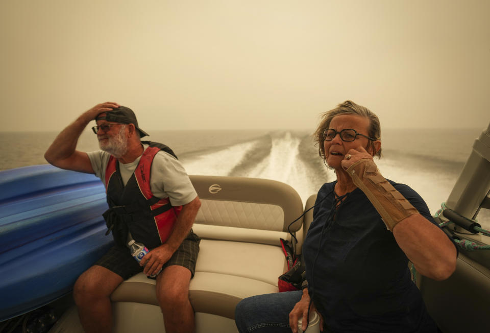 Smoke fills the air as Trevor Manzuik and his wife Pat are given a boat ride by good samaritan Christy Dewalt, not seen, back to their home they were evacuated from due to the Lower East Adams Lake wildfire, in Scotch Creek, Canada, Sunday, Aug. 20, 2023. (Darryl Dyck/The Canadian Press via AP)