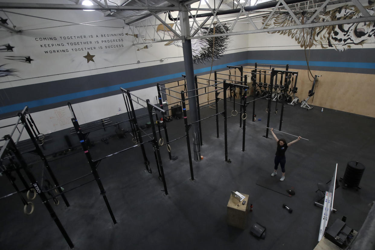 FILE - In this April 24, 2020, file photo, Alexis Garrod, CrossFit Potrero Hill partner and head coach, demonstrates an exercise to participants while instructing a class over Zoom in an empty gym, which closed for shelter-in-place orders during the coronavirus outbreak in San Francisco. California will allow schools, day camps, bars, gyms, campgrounds and professional sports to begin reopening with modifications starting Friday, June 12, 2020. (AP Photo/Jeff Chiu, File)