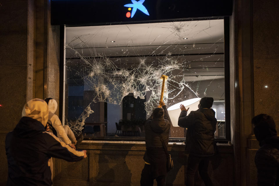 Demonstrators smash the window of a bank following a protest condemning the arrest of rap singer Pablo Hasél in Barcelona, Spain, Thursday, Feb. 18, 2021. Protests over the imprisonment of a rapper convicted for insulting the Spanish monarchy and praising terrorist violence have morphed for the third night in a row into rioting. Pablo Hasél began this week to serve a 9-month sentence in a northeastern prison. (AP Photo/Felipe Dana)