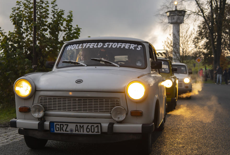 Legendary GDR Trabant (Trabi) cars,drive in front of a control tower of the former GDR border guard forces during a symbolic wall opening, celebrating the 30th anniversary of the falling wall in the outdoor area of the German-German museum in Moedlareuth, Germany, Saturday, Nov. 9, 2019. Moedlareuth, named 'Little Berlin', was the symbol of a divided village along the borderline between East and West Germany. The border ran straight through the little village. (AP Photo/Jens Meyer)
