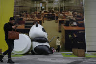 People walk by a sculpture depicting a working panda on display near a billboard promoting office space on a vacant lot at a commercial office building in Chengdu in southwestern China's Sichuan Province on Feb. 27, 2024. China's efforts to restore confidence and rev up the economy will top the agenda during this month’s meeting of the ceremonial national legislature. (AP Photo/Andy Wong)