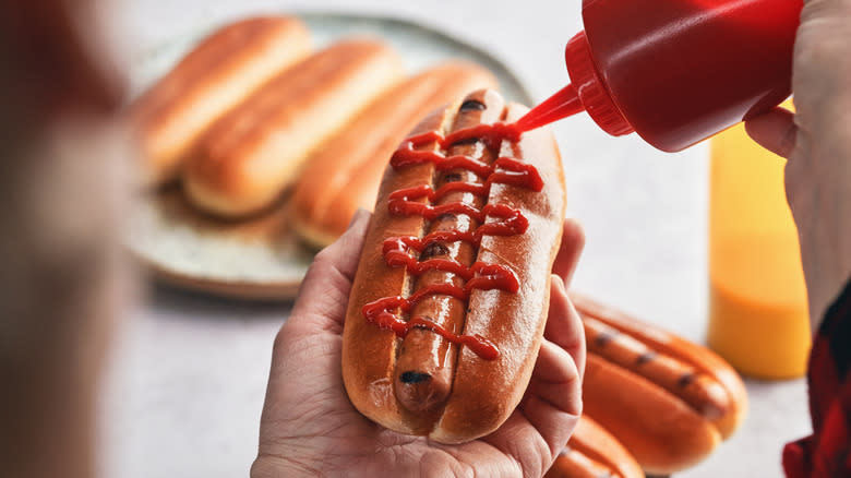 adding ketchup to hot dog