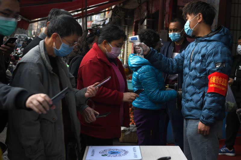 People wearing face masks scan a QR code to submit their personal information while security volunteers check their temperatures at an entrance of a grocery market, as the country is hit by an outbreak of the novel coronavirus, in Kunming