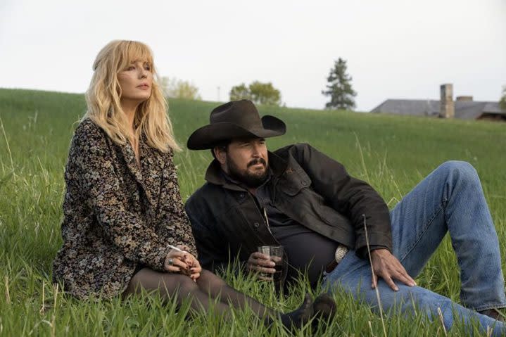 A woman sits down next to a man lying down on a hill.