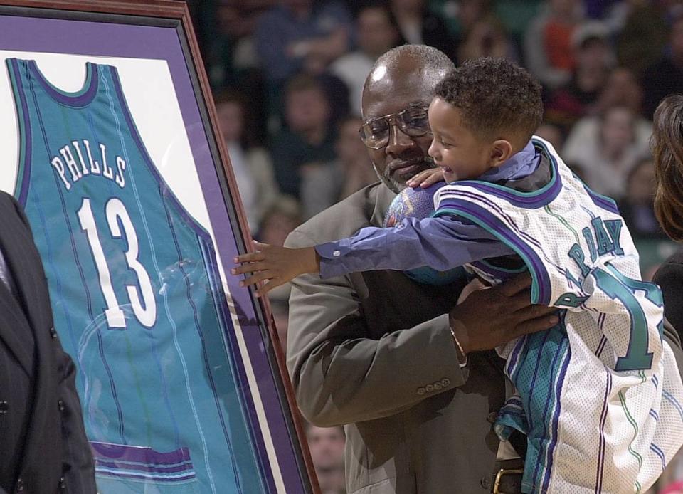 Trey Phills, then 3, reaches around his grandfather, Bobby Sr., to touch his father’s Hornets jersey during a ceremony to retire the number at the Charlotte Coliseum in February 2000.
