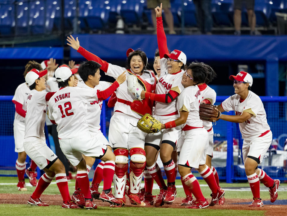 Japanese women's softball team celebrates on the field, smiling and hugging after a game