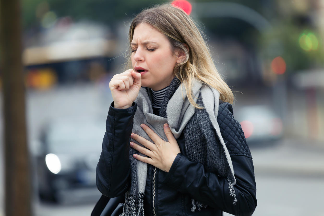 Shot of illness young woman coughing in the street.