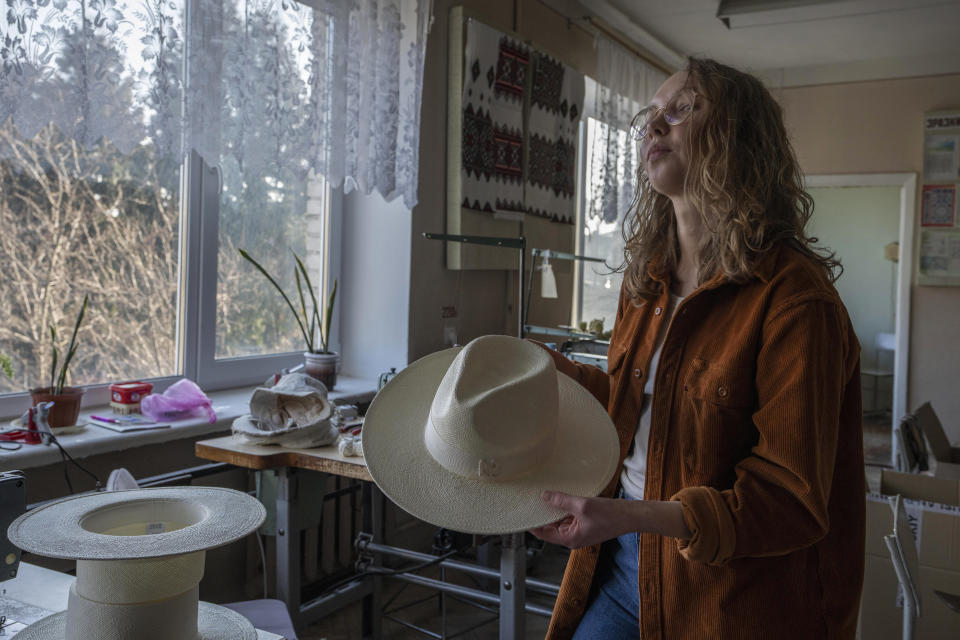 Ukrainian co-founder and whole sale director Victoria Semerei, of high-end hat designer brand Ruslan Baginskiy 'RB', shows a handmade hat, inside a college classroom turned into a workshop the company has been working from in Lviv, western Ukraine, Friday, March 25, 2022, after fleeing Kyiv. (AP Photo/Nariman El-Mofty)