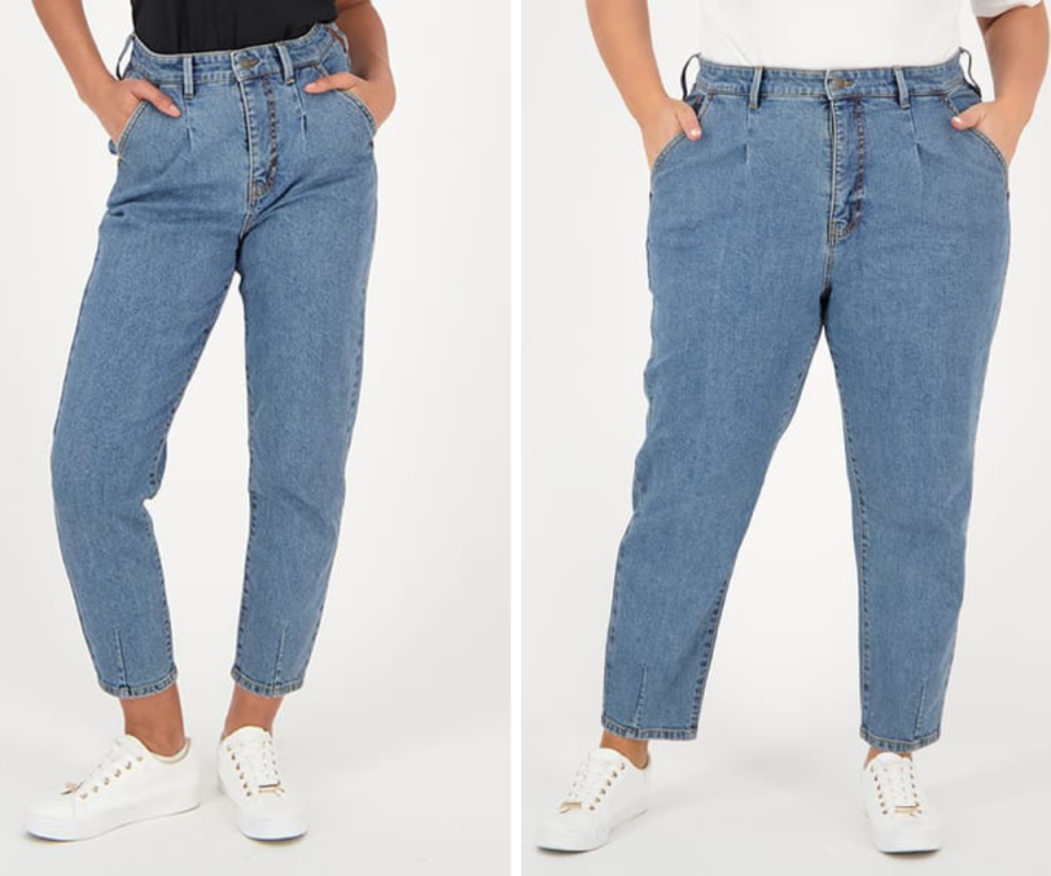 A thin woman on the left wears blue tapered ankle length, high waisted jeans with white trainers while a plus size woman on the right wears the same jean against a whiteb background.