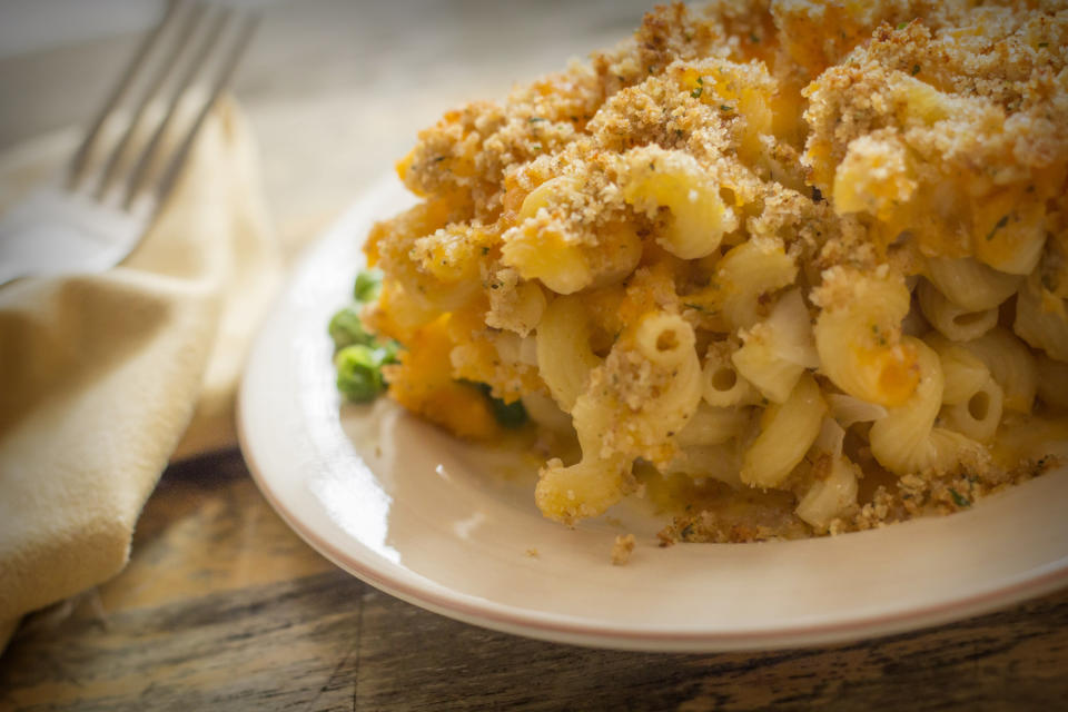 A plate of mac and cheese with a breadcrumb topping, sitting on a wooden table beside a fork and napkin