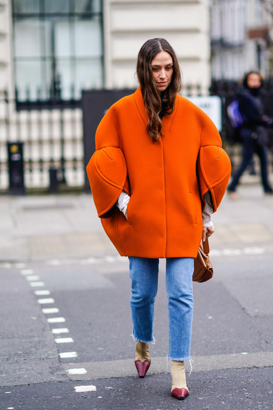 A guest wears an orange oversized coat during London fashion week in February.