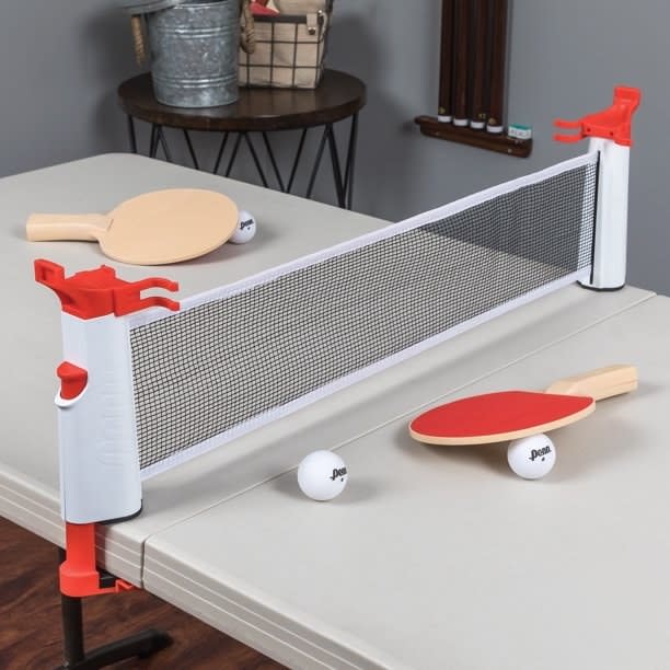 portable table tennis set set up over a folding table with a net, two paddles, and three balls