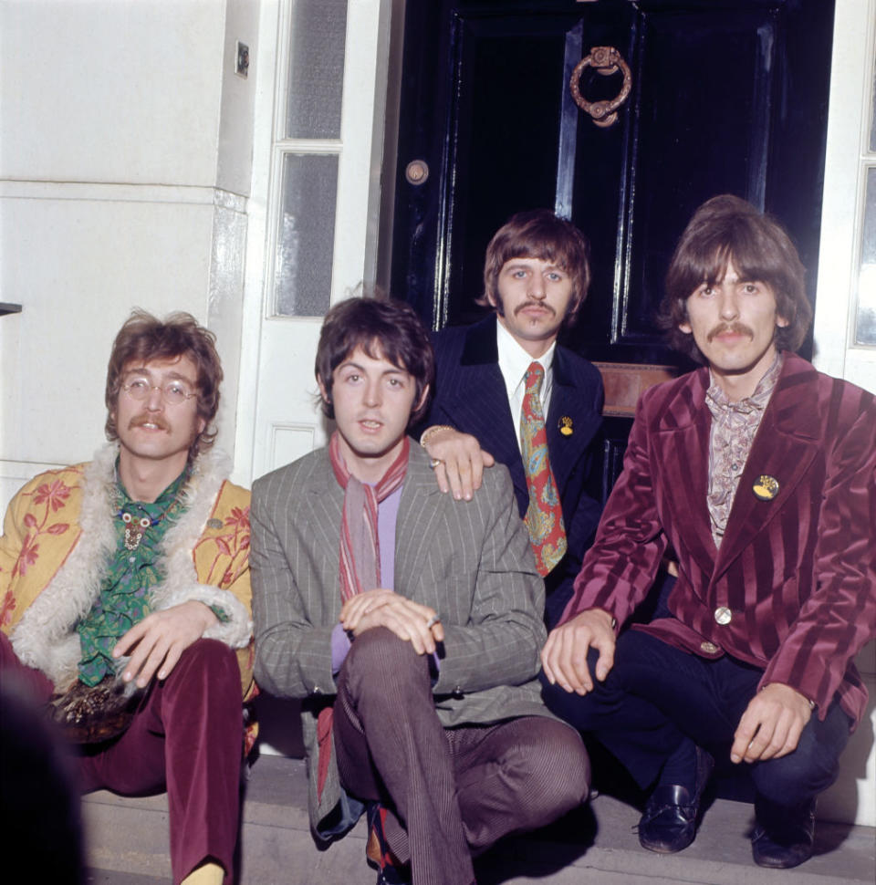 John Lennon, Paul McCartney, Ringo Starr, and George Harrison are sitting on stairs wearing stylish, colorful 1960s attire