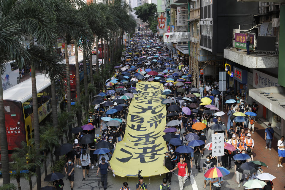 Protesters walk next to a banner with the words "May Glory be to Hong Kong" in Hong Kong on Saturday, Oct. 5, 2019. All subway and trains services are closed in Hong Kong after another night of rampaging violence that a new ban on face masks failed to quell. (AP Photo/Vincent Thian)