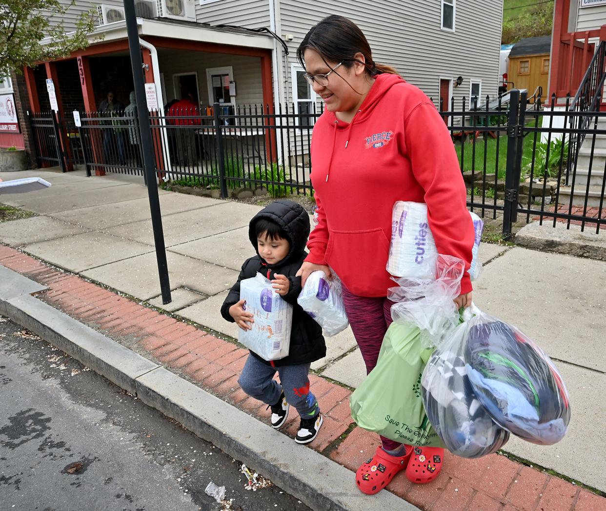Maria Chuqui and her son, Andrew, 3, cross Millbury Street after getting bags of food, clothes and diapers at Pernet Family Health Service.