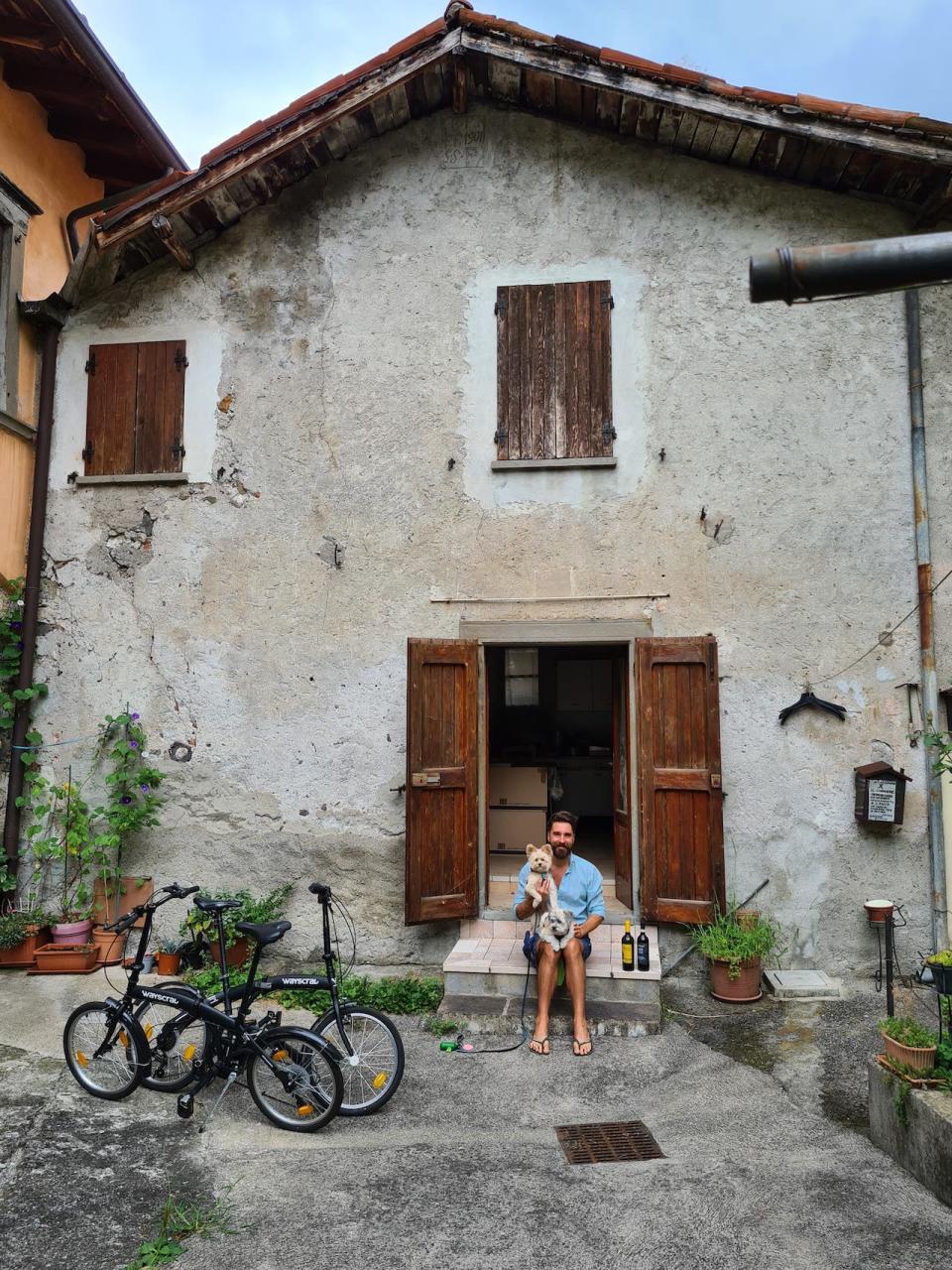 A man sitting outside a home in Italy with two dogs.